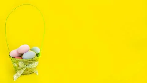 Wide Easter banner. Green basket with colorful eggs on a yellow background. Stock Photos