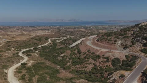 Wide elevated view of a winding paved road crossing a dry hilly coastal Stock Footage 344141002