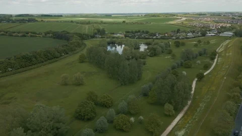 Wide flight over a tree lined lake with plush gardens passing over a road Stock Footage 297175143