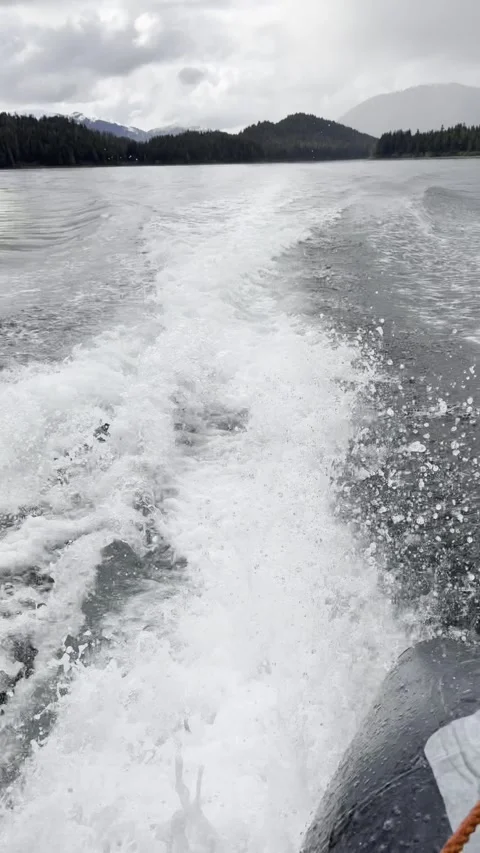 Wide Foaming Wake Trailing a Skiff Past Forested Shores, Cloudy Peaks, Vertical Stock Footage 336220589