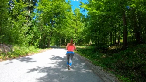 Wide forward tracking shot of an overweight woman running on the sunny road Stock Footage 109371706