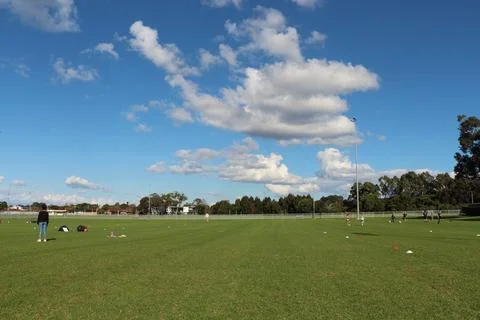 Wide Green Grass Field Under Clear Blue Sky With Clouds And Football Training Stock Photos