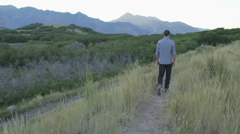 Wide Handheld of Man Walking Down Path Touching Weeds with Hand (Moutains in  動画素材 68723670