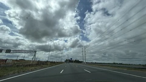 Wide highway stretching under dramatic cloud cover with power lines, roadside Stock Photos