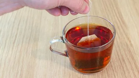 Wide horizontal composition of hand dipping tea bag into glass cup Stockfoto's