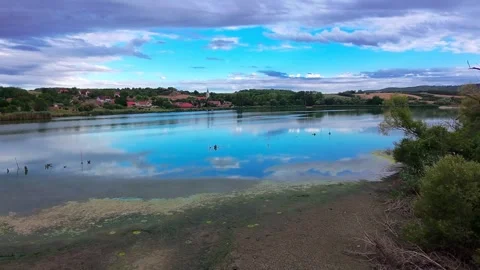 Wide Horizontal Pan Shot Over Lake Water Sky Reflection and Village Skyline in 스톡 동영상 345100604