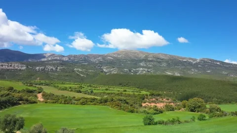 Wide landscape view of green fields and rolling hills with rugged mountains in Stock Footage 346670743