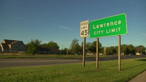Wide of Lawrence, KS Sign with Speed Limit Sign and Cars Passing Stock Footage