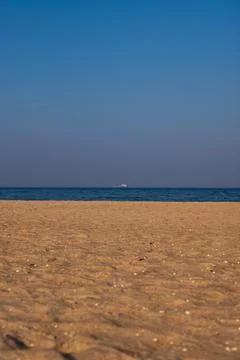 Wide low angle sandy beach and distant ship under clear sky Stock Photos