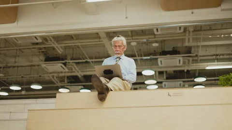 Wide low angle of senior Thai man using laptop atop wooden bleachers Vídeos de archivo 347777926