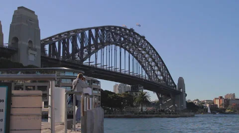 A wide low angle shot of the Sydney harbour bridge and moving dock with man Stock Footage 36686099
