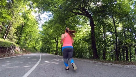 Wide low angle tracking shot of an overweight woman running on the sunny road Stock Footage 109372592