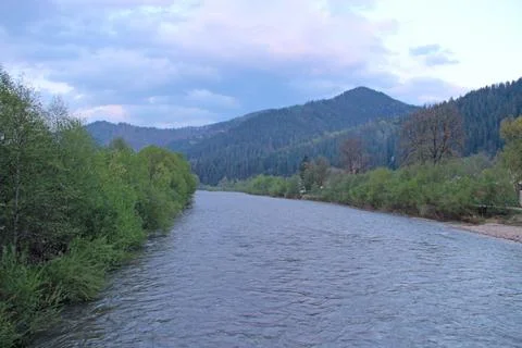 Wide mountain river flowing through a green valley under a cloudy evening sky Stock-Fotos