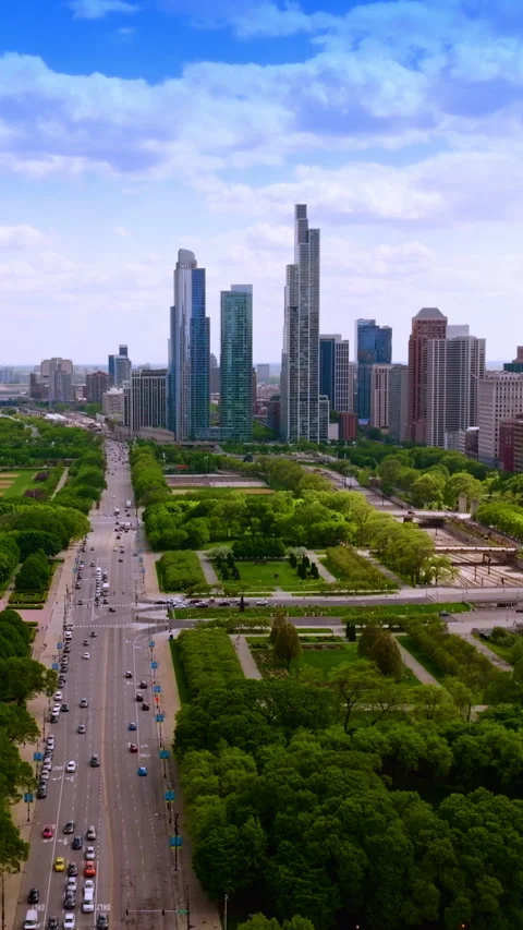 Wide multi-lane road with numerous cars passing through green park zone.  Vidéo 265800967