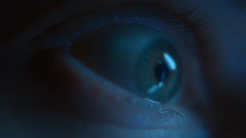 Wide-open human eye madly staring at a glowing screen at night Stock Footage 318960438