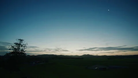 Wide Pan of sun setting behind mountain range with blue sky Stock Footage 153239186