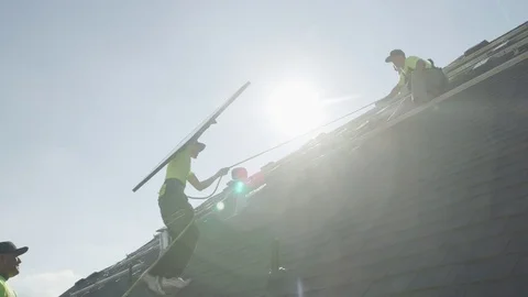 Wide panning low angle shot of workers carrying solar panel on roof / Mapleton, Stock Footage 77469195