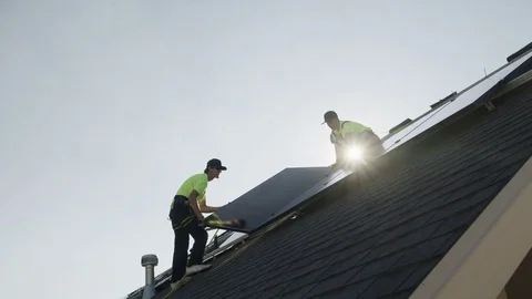 Wide panning low angle shot of workers installing solar panel on roof / Stock Footage 77469406