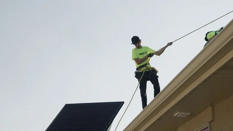 Wide panning low angle shot of workers carrying solar panel on roof / Mapleton, Stock Footage 77469426