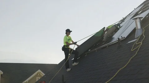 Wide panning low angle shot of worker installing solar panel on roof / Mapleton, Stock Footage 77469456