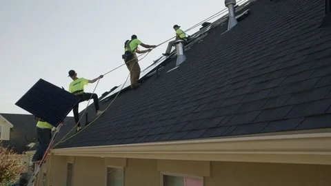 Wide panning low angle shot of workers carrying solar panel on roof / Mapleton, Stock Footage 77469501