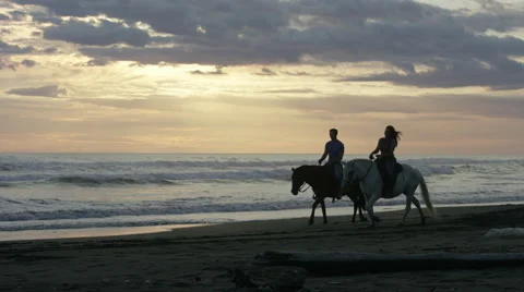 Wide panning shot of couple riding horseback on beach / Esterillos, Puntarenas, Stock Footage