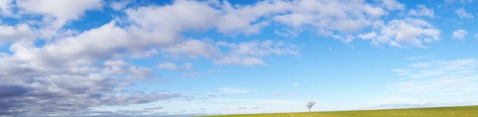 Wide panoramic view of blue skies and white scattered clouds and green ground Stock Photos