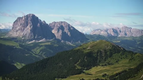 Wide panoramic view of Dolomites mountain peaks above green valleys under blue Vidéo 318664490