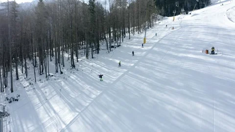 Wide panoramic view of a snow-covered ski slope surrounded by a dense forest. Видео 285900524