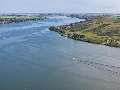 Wide river flows past grassy banks, boat glides calmly beneath clear sky Stock Photos