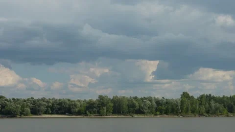 A wide river flows past a green forest under dramatic clouds. Stock Footage 341689366