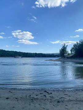 Wide river flows under blue sky with distant boat, forested banks Stock Photos