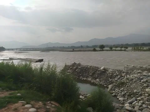 A wide river flows under a bridge with mountains Stock Photos