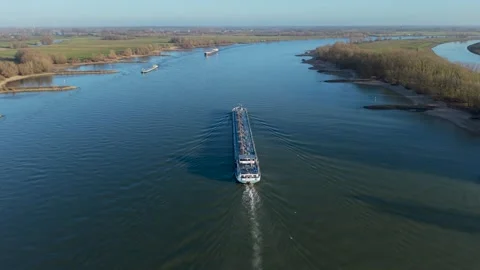 Wide river with multiple cargo ships moving along calm water, surrounded Stock Footage 329076348