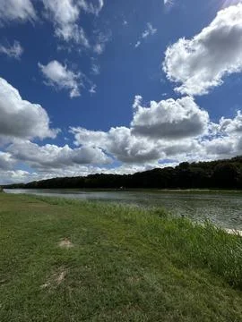 Wide riverside landscape with dramatic white clouds over blue sky, grassy Fotos Stock