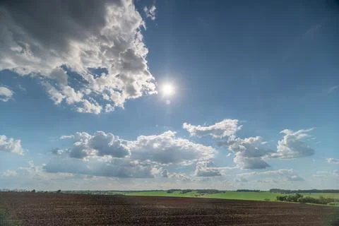 Wide rural field under dramatic blue sky with sun and clouds Stock Photos