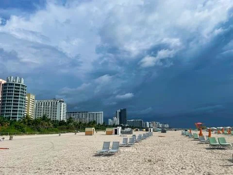 Wide sandy beach lined with empty lounge chairs facing modern coastal skyline Stock Photos