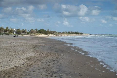 Wide sandy beach with ocean waves and scattered people in the distance Stock Photos