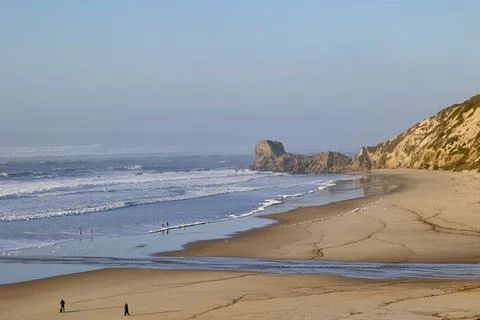 Wide sandy beach with waves and rocky coastline Stock Photos