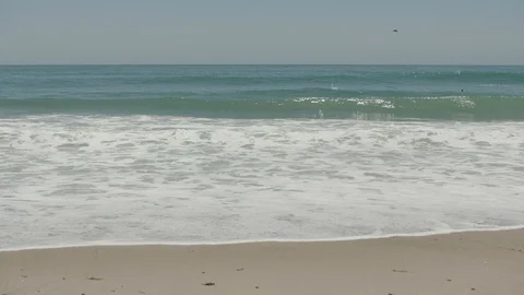 WIDE SHOT OF BEACH AND WAVES CRASHING IN SLOW MOTION WITH SURFERS Stock Footage 127470911