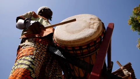Wide shot of black man hitting skin of dundun with wooden stick Stock Footage 113166149