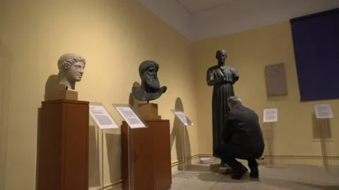 Wide shot of blind man touching a copy of the charioteer of Delphi Stock Footage 140988083