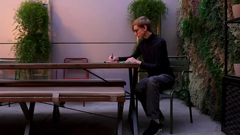 A wide shot of a creative guy sketching with a pen in a sketchbook outdoors Stock Footage 346130981