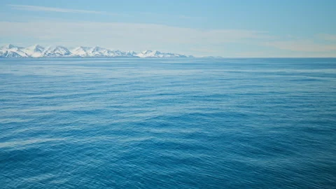 Wide shot of deep blue ocean with distant snow-covered mountains, in Iceland. Stock Footage 293635870
