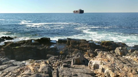 Wide shot, distant container ship, shoreline black rocks, horizon 스톡 동영상 102610596
