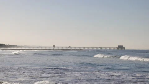 Wide shot of distant ocean pier with surfers Stock Footage 170380602