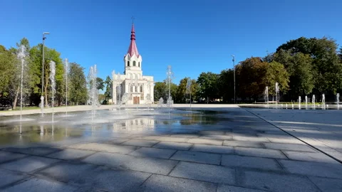 Wide shot of dry deck walkable fountain in city square, church in background Vídeos de archivo 280487528