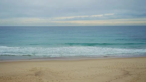 Wide shot empty beach with footprints on sand and small waves in ocean in winter Stock Footage 287301469