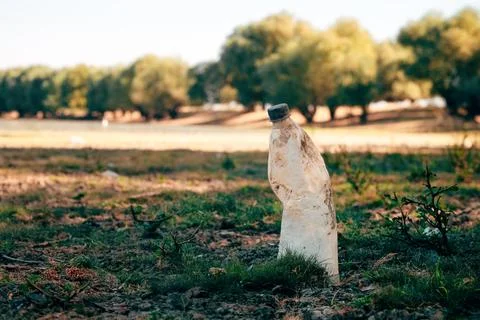 A wide shot of an empty clear plastic bottle lying discarded on dry, patchy.. Stockfoto's