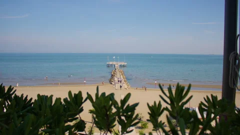 Wide shot of an empty sandy beach, with calm sea, long pier and greenery Stock Footage 295909059